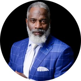 Portrait of Myron Golden wearing a blue suit and white tie, looking confident