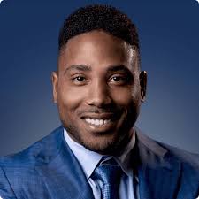 Professional headshot of Karlton Dennis in a blue suit, smiling against a dark blue background